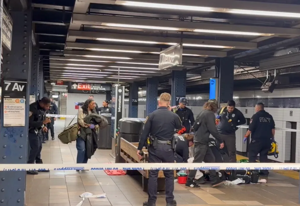 Police officers and other personnel gather on a subway platform cordoned off with crime scene tape following a shooting.