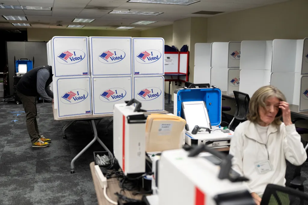 A person casts their vote during early voting at a polling place in Virginia, with voting booths and equipment visible in the room.