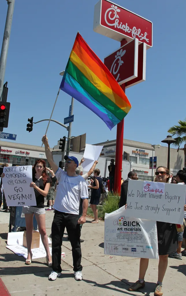 Demonstrators hold signs and a rainbow flag during a protest outside a Chick-fil-A restaurant.