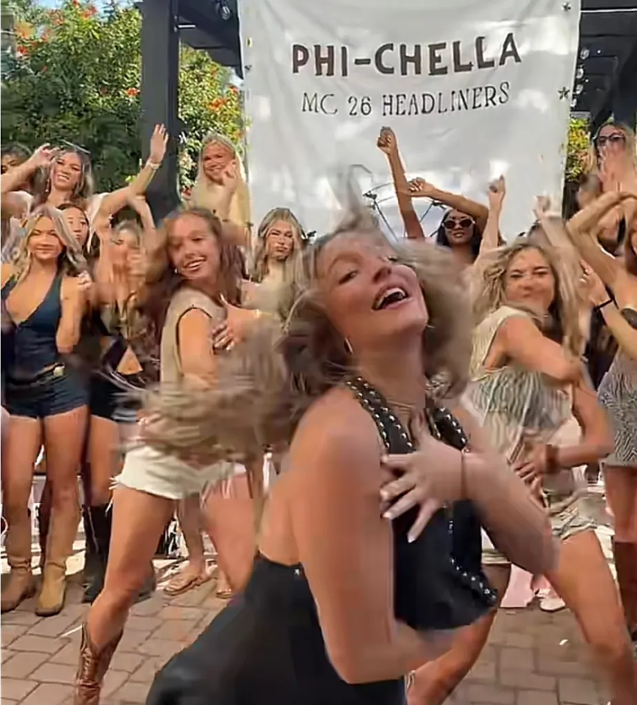 A group of young women dancing outdoors in front of a banner that reads 