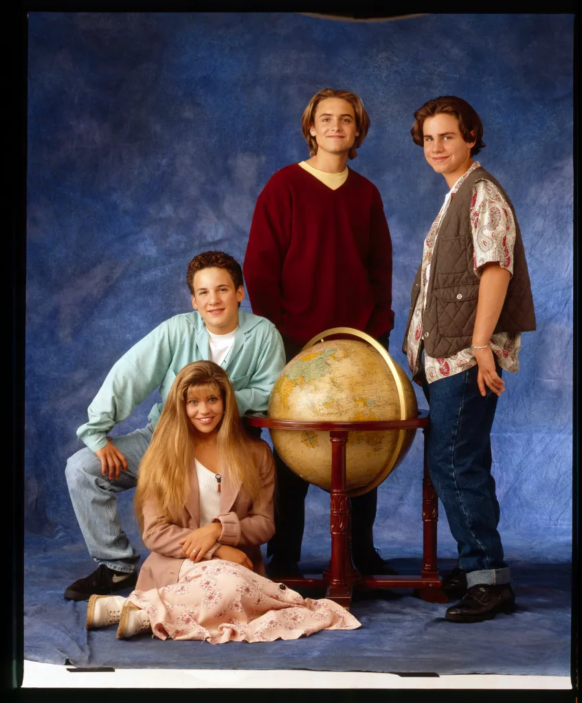 Cast members Danielle Fishel, Ben Savage, Will Friedle, and Rider Strong pose with a globe in a promotional photo for Boy Meets World.