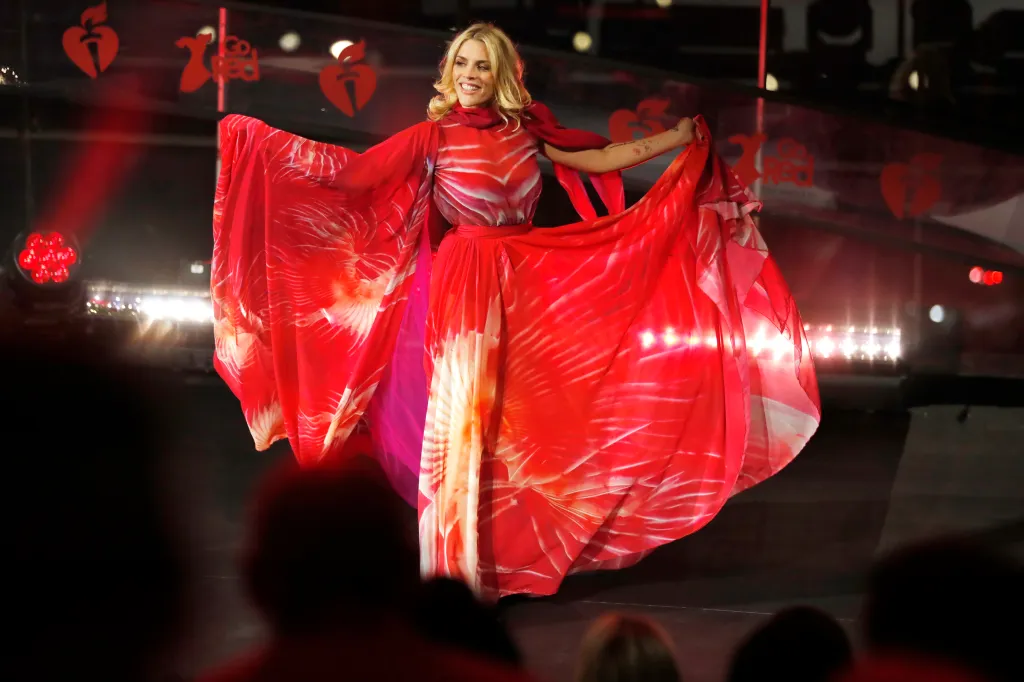 Busy Philipps poses onstage in a flowing red dress during the Red Dress Collection Concert.