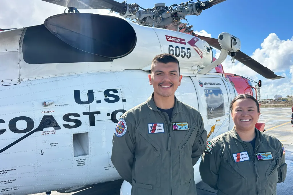 U.S. Coast Guard officer Josh Law and Lt. Miyako Miller stand in front of a rescue helicopter.