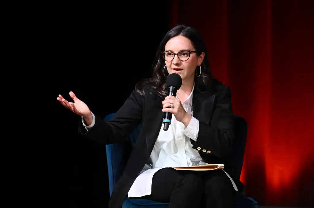Bari Weiss speaks onstage holding a microphone and gesturing with her hand.