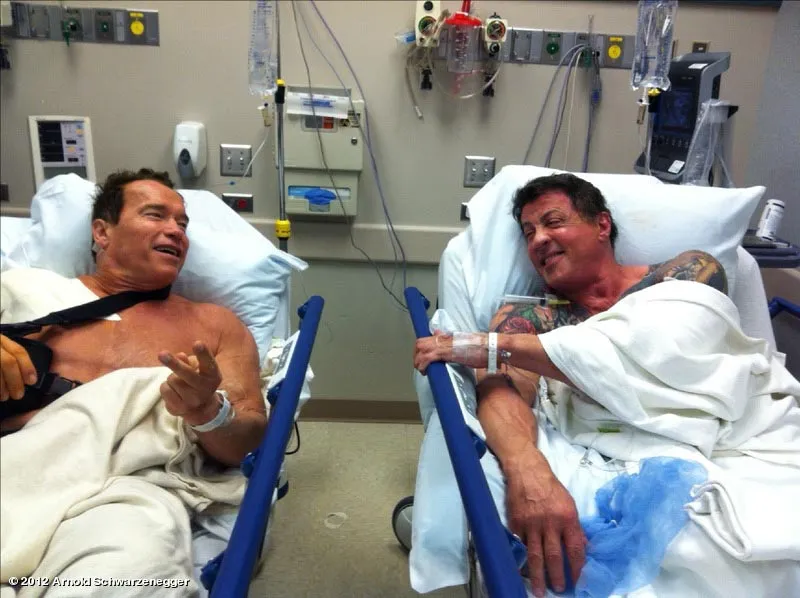 Sylvester Stallone and Arnold Schwarzenegger lie next to each other in hospital beds before their shoulder surgeries.
