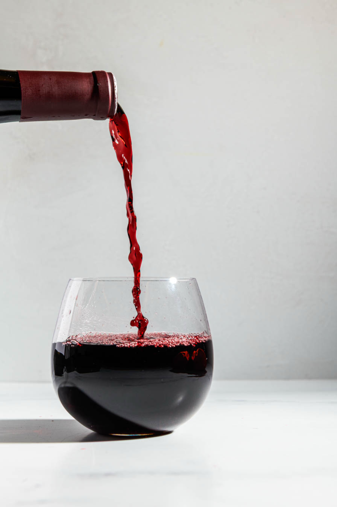 Red wine being poured from a bottle into a stemless glass.