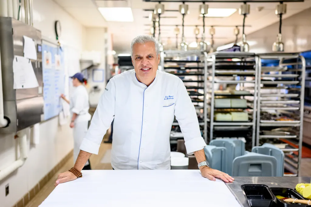Chef Eric Ripert smiles while standing in a commercial kitchen.