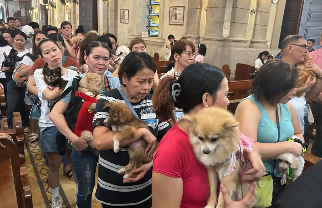 Pet owners stand in a line holding their dogs and cats during animal blessing rites inside a church.