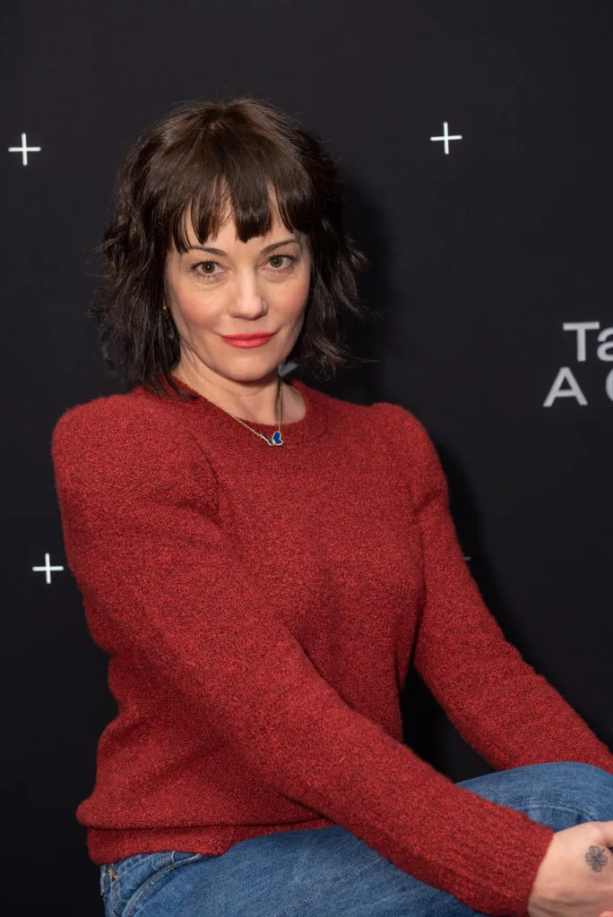 Natasha Gregson Wagner wearing a red sweater and blue jeans.