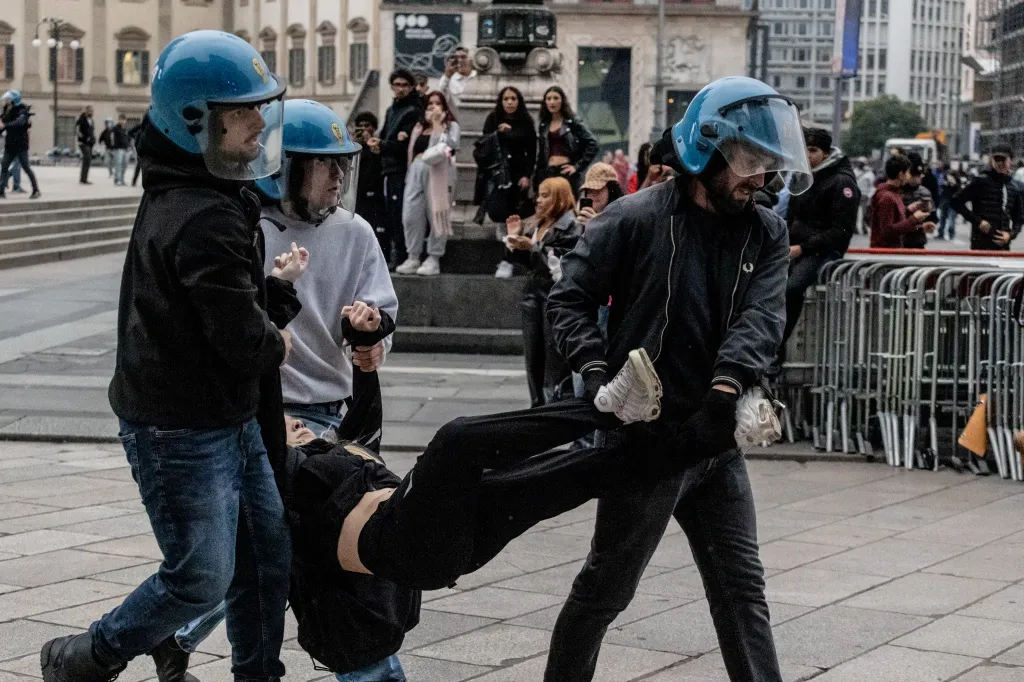 Police officers in blue helmets carrying a protester during urban unrest in Milan.