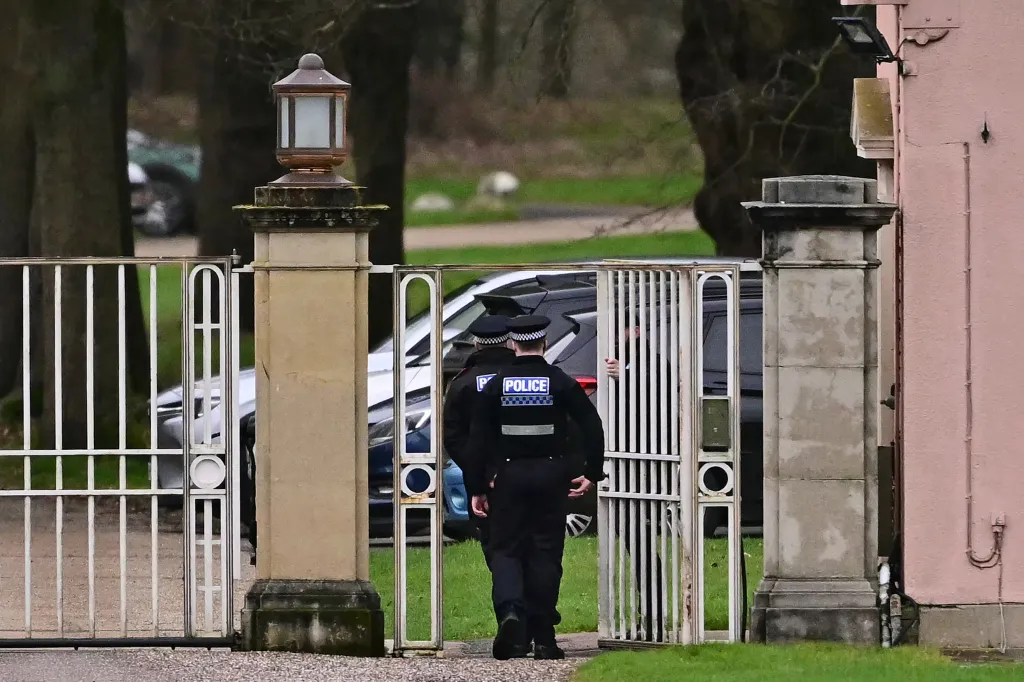 Police officers walk through the gated entrance to Royal Lodge.