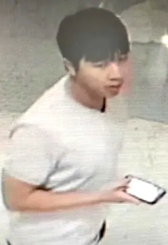 Surveillance image of a male suspect in a white t-shirt holding a phone.
