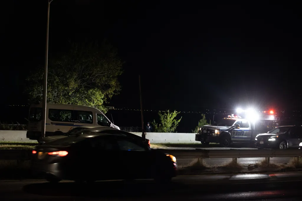Police vehicles and officers investigate the scene of a stabbing at night along the Belt Parkway in Brooklyn.