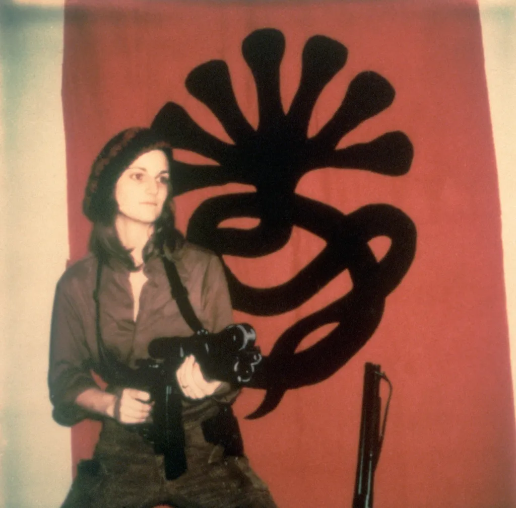 Patty Hearst poses with a machine gun in front of a Symbionese Liberation Army flag in 1974.
