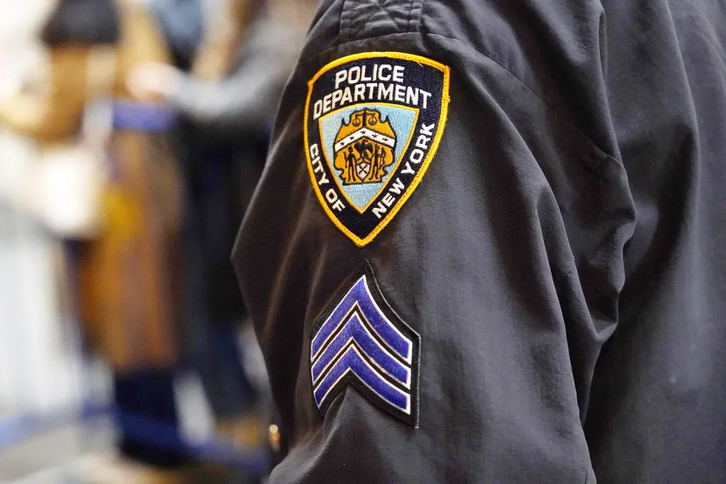 An NYPD sergeant chevron arm patch is sewn onto the sleeve of a dark uniform.