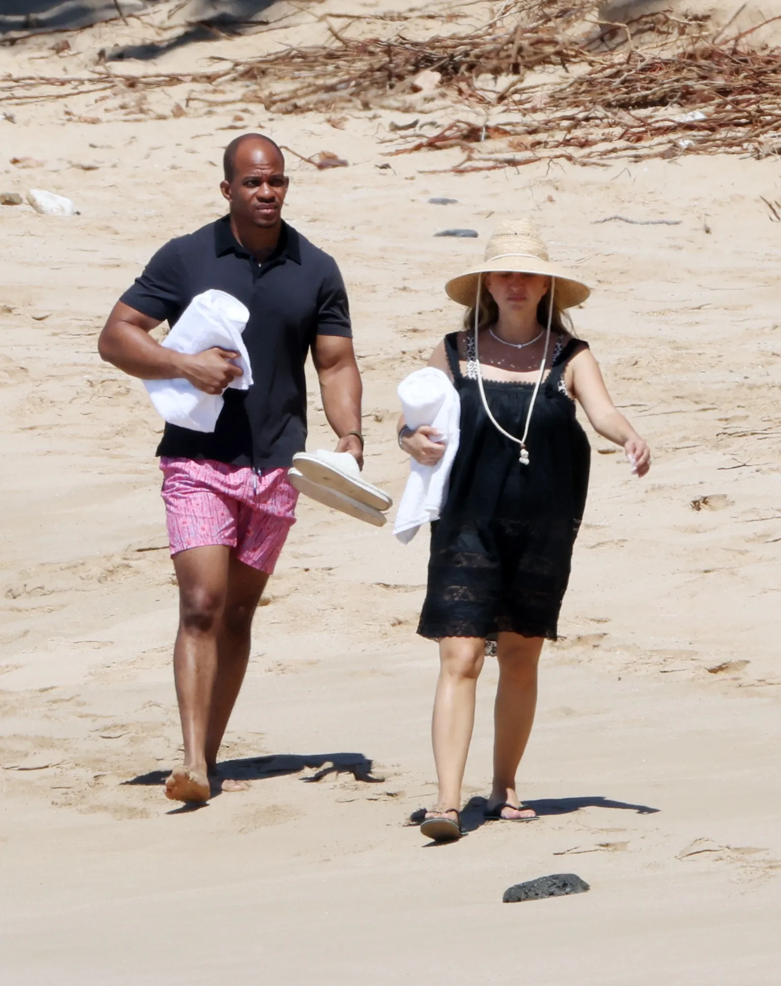 Jennifer Meyer and Geoffrey Ogunlesi walking on a beach in Hawaii, each carrying a white towel.