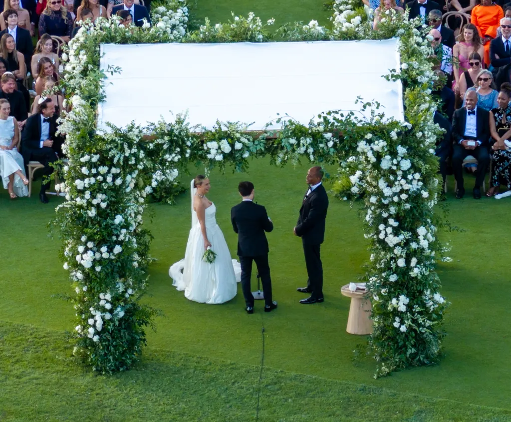 Jennifer Meyer and Geoff Ogunlesi stand beneath a white floral chuppah during their wedding ceremony.