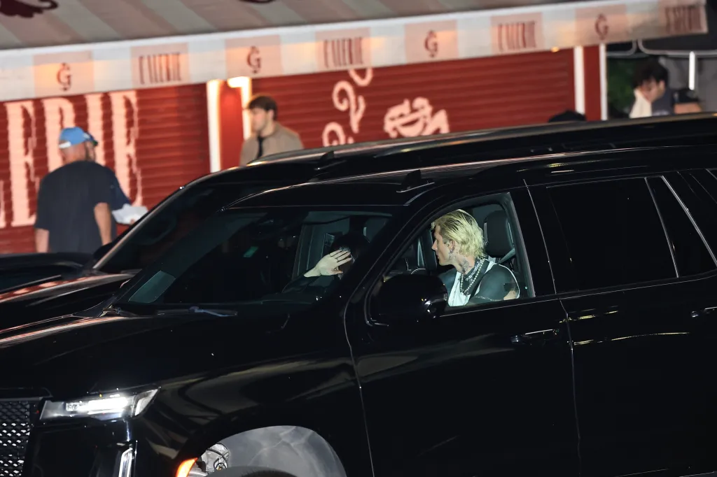 Machine Gun Kelly and Dakota Johnson sitting inside a black SUV at night.