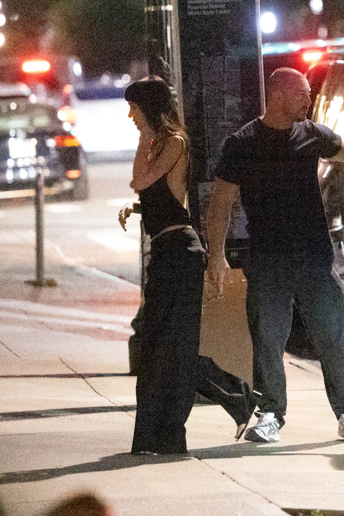 Dakota Johnson walking on a New York City street at night, accompanied by security.