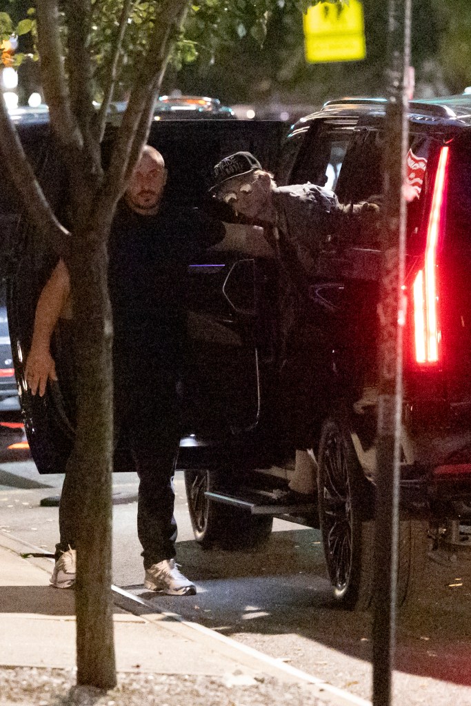 MGK stepping out of a black SUV at night, assisted by a security guard.
