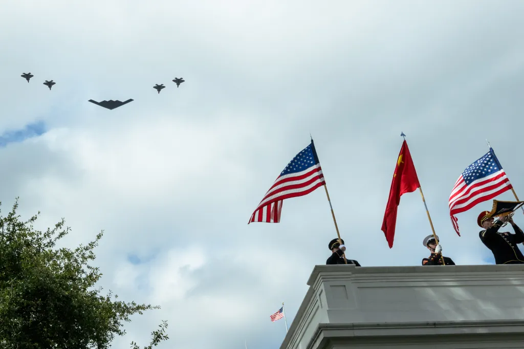 U.S. and Chinese flags are held on a White House colonnade while a B-2 bomber and four fighter jets fly overhead.