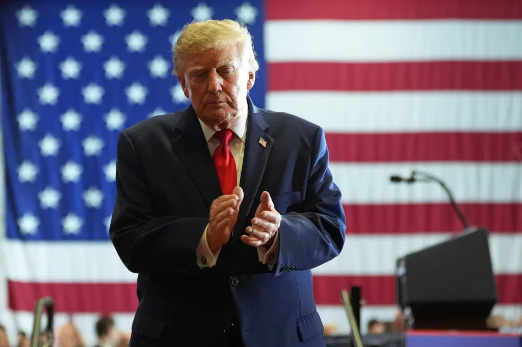 President Donald Trump claps at a campaign rally in front of an American flag.