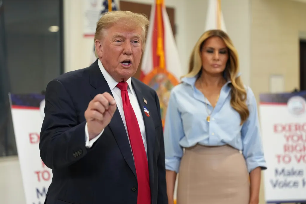 Donald Trump speaks with his hand raised, alongside first lady Melania Trump.