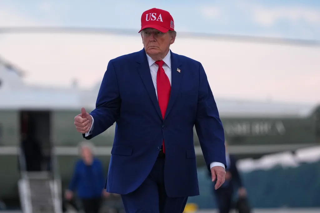President Donald Trump wearing a red USA hat and giving a thumbs-up.