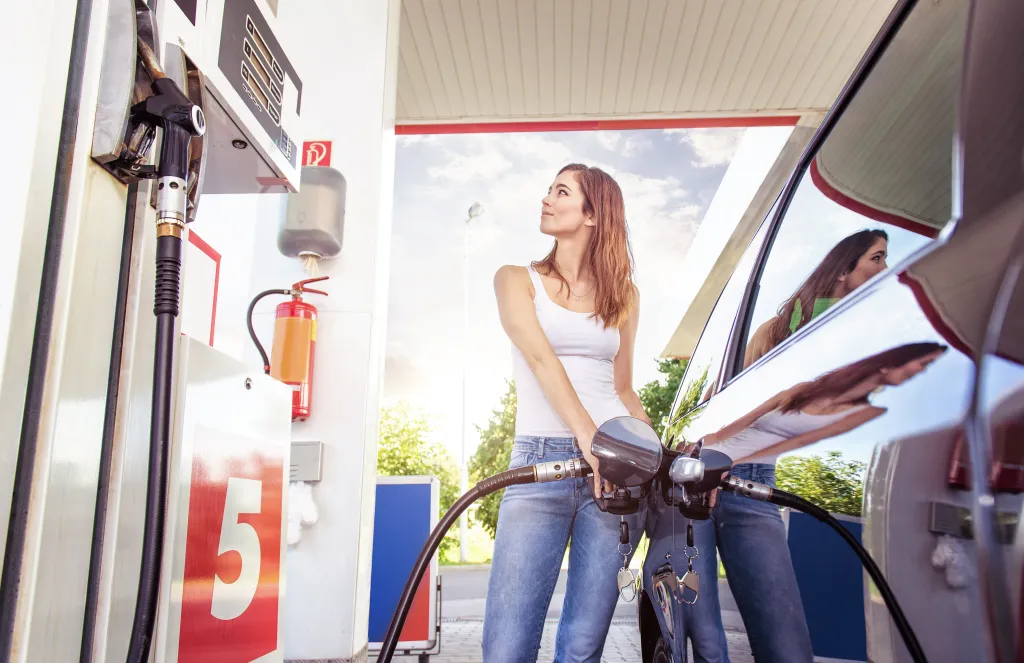 A young woman refuels her car at a gas station.