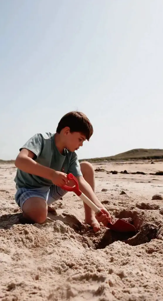 Prince Louis playing in the sand with a toy shovel on a beach.