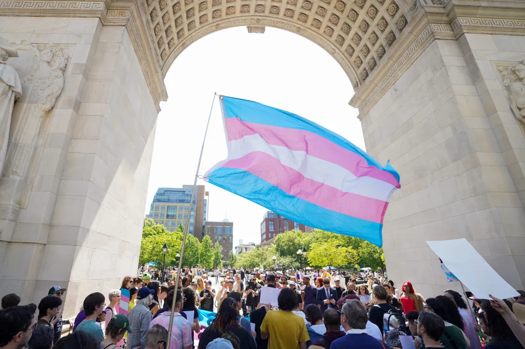 A large crowd gathers beneath the Washington Square Arch in Manhattan, holding a transgender pride flag during the 