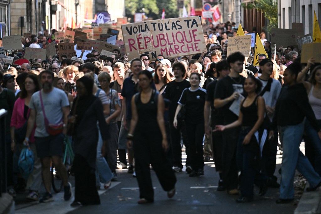 A large crowd of high-school students marches down a street, holding placards during a protest over learning conditions.