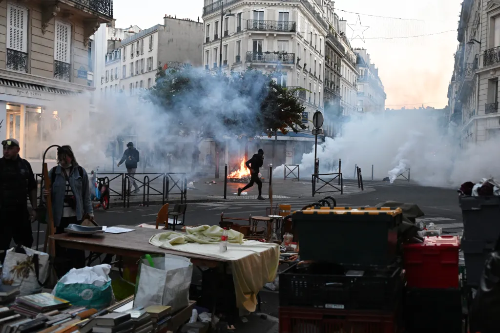 A protester runs through tear gas while a flea market takes place amid clashes in Paris.