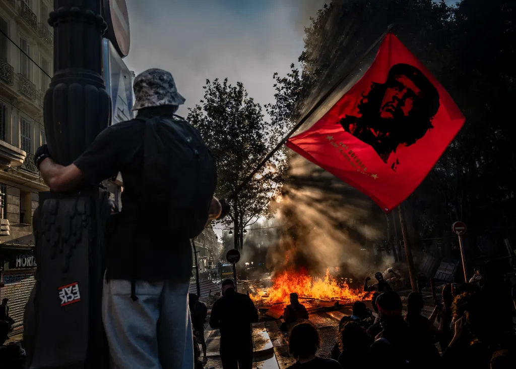 A protester waves a red flag bearing a portrait of Che Guevara in front of a burning barricade during clashes at a protest in Marseille, France.