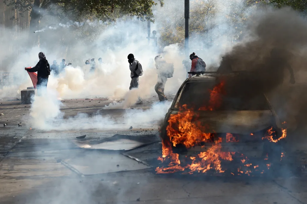Protesters stand near a burning car and thick smoke during a demonstration in Paris.