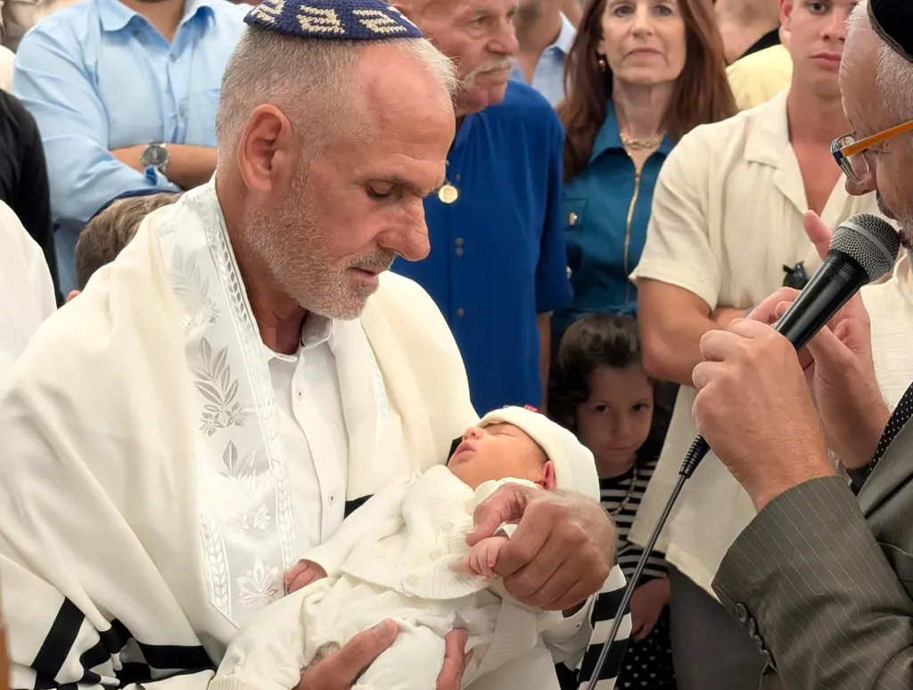 Yigal Sarusi holding his newborn son, Lavi, at his bris surrounded by family and friends.