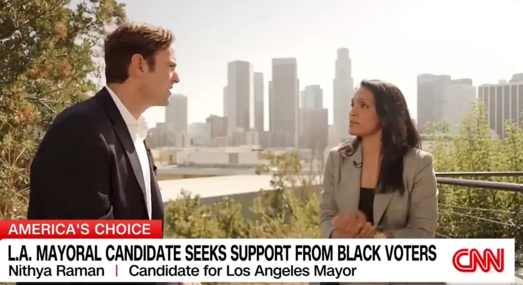 Nithya Raman being interviewed outdoors with the Los Angeles skyline in the background.