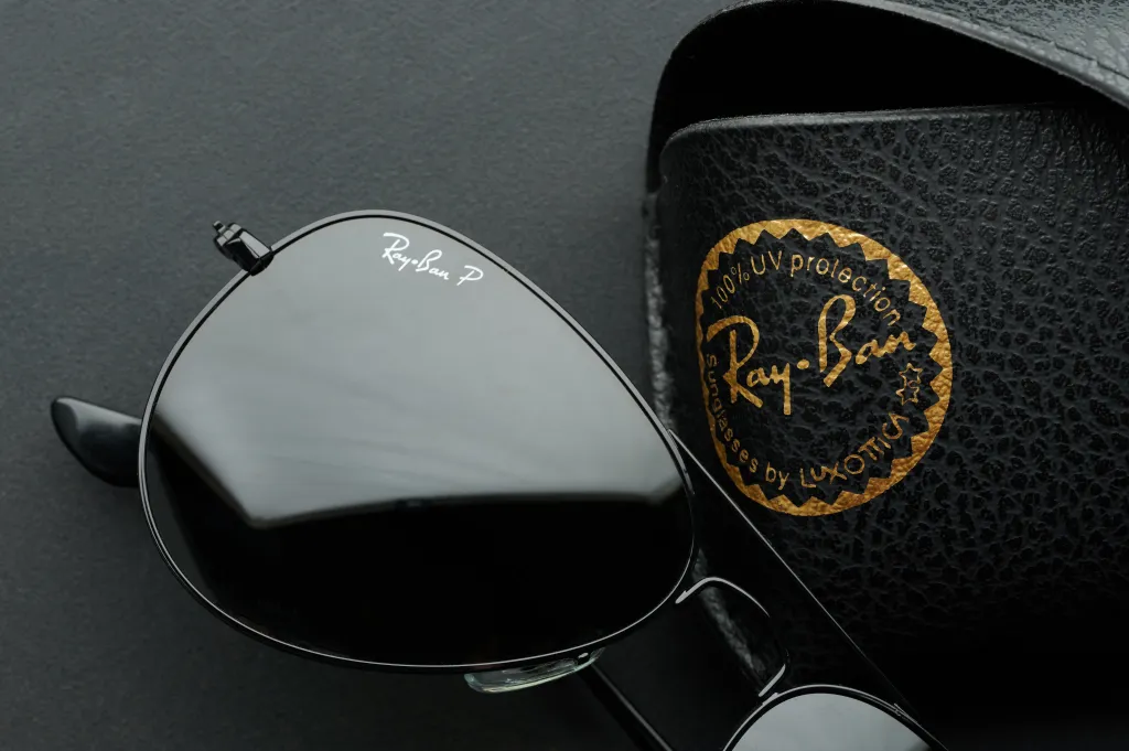 A Ray-Ban sunglasses lens next to its case on a black metal background.