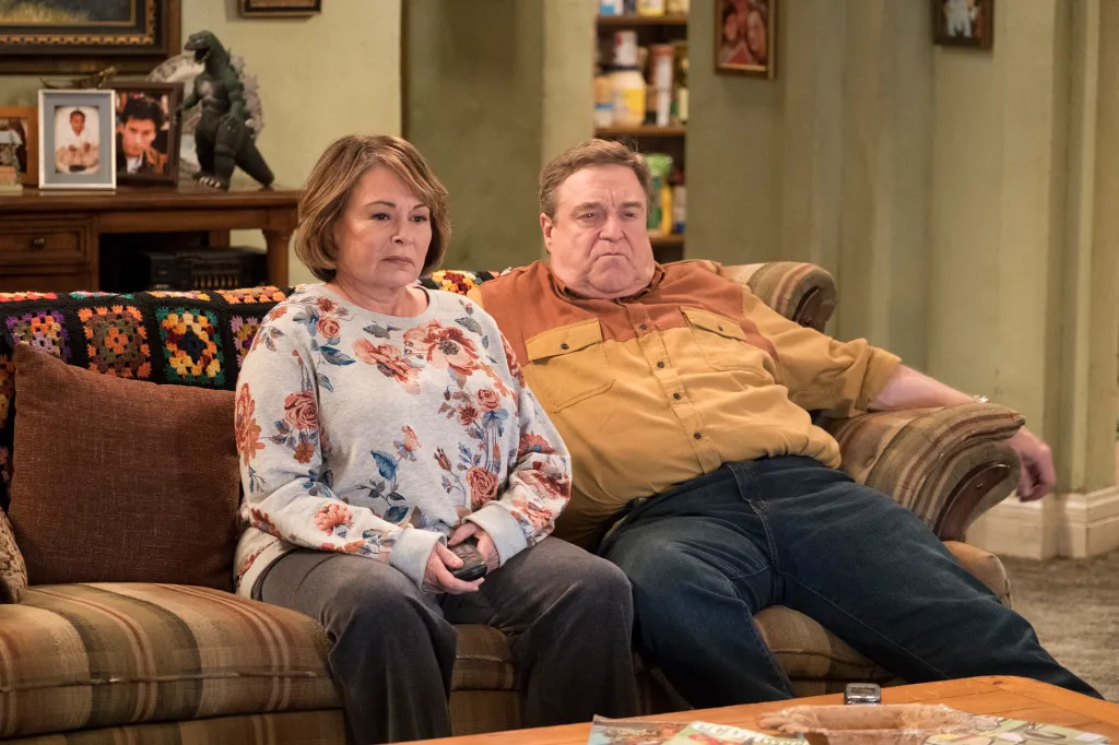 Roseanne Barr and John Goodman sitting on a sofa in a scene from the television show 