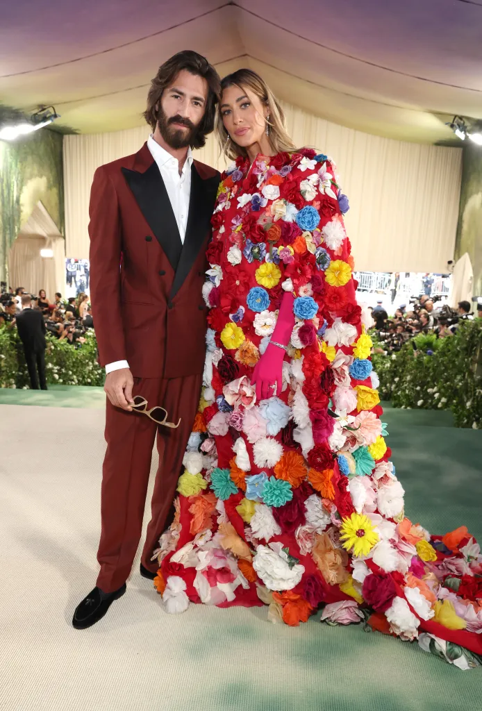 Leonardo Del Vecchio in a burgundy suit and Jessica Serfaty Michel in a red gown covered in colorful artificial flowers at the Met Gala.