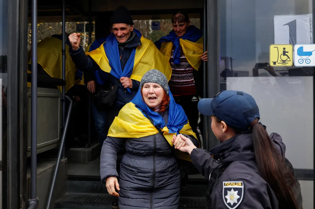 Residents evacuated from the Russian-occupied town of Oleshky arrive in Ukrainian-controlled territory, draped in Ukrainian flags and greeted by a police officer.