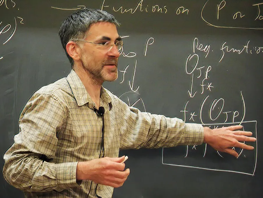 Mathematician Richard Borcherds stands in front of a chalkboard covered in mathematical equations, pointing at the board.