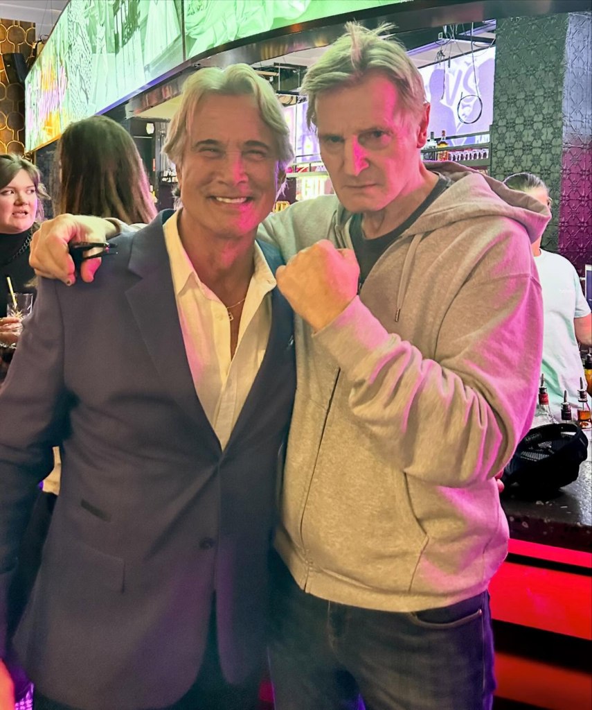 Richard Norton and Liam Neeson pose together, with Neeson making a playful fist at the camera.
