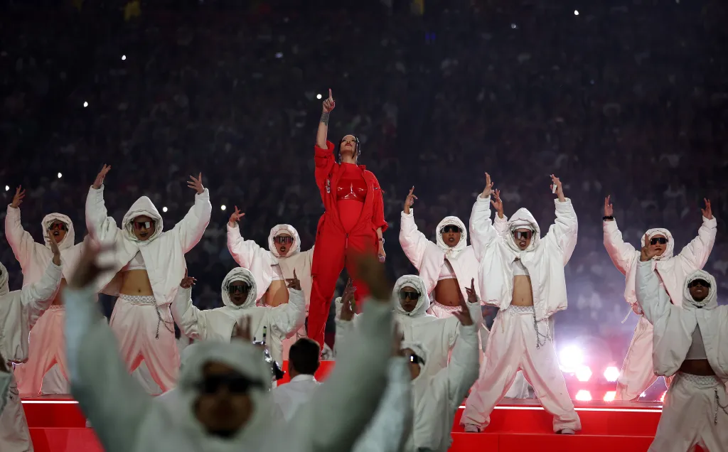 Rihanna performs onstage in a red jumpsuit with backup dancers in white outfits at the Super Bowl LVII Halftime Show.