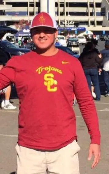 Portrait of Robert Rocha wearing a red USC long-sleeve shirt and matching cap outdoors.