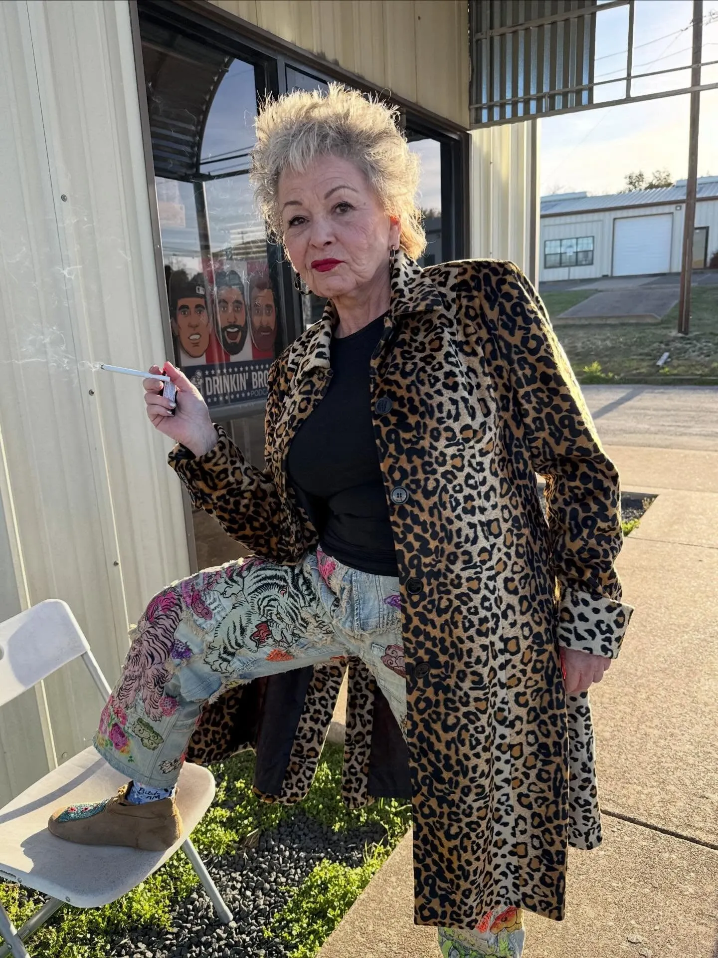 Roseanne Barr wearing a leopard print coat and embroidered jeans while smoking a cigarette.