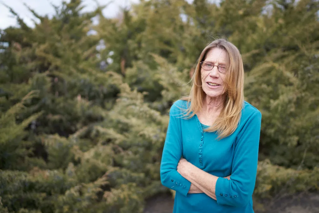 Roslyn Markle stands with her arms crossed in front of a green bush.
