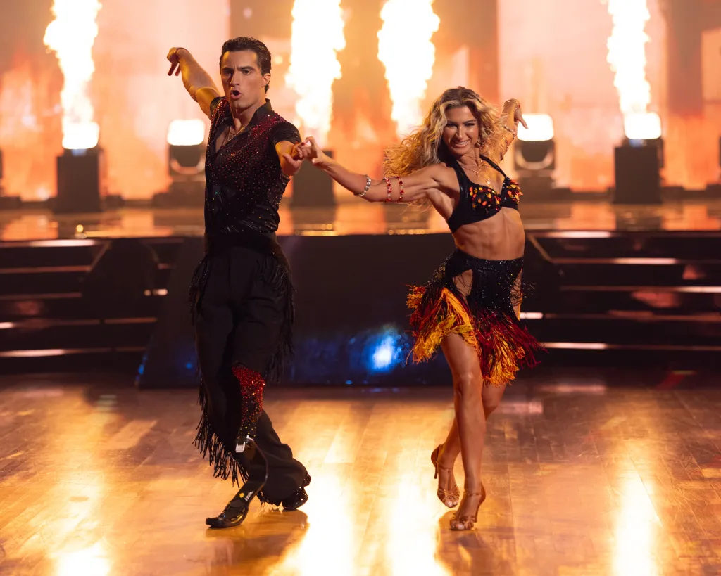Ezra Frech and Daniella Karagach dance on a stage with fiery pyrotechnics in the background.