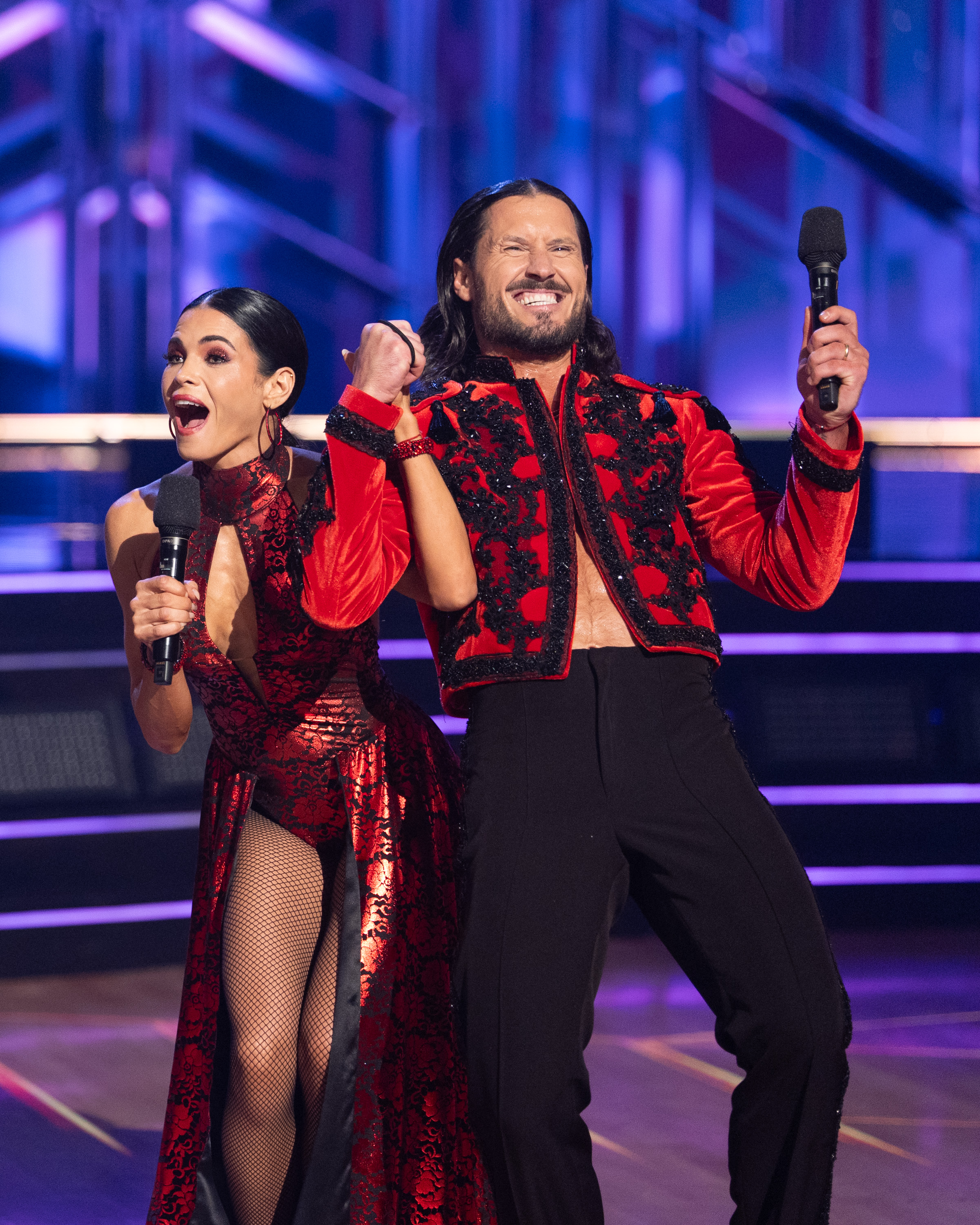 Jenna Dewan and Valentin Chmerkovskiy hold microphones and smile excitedly on the Dancing with the Stars stage.