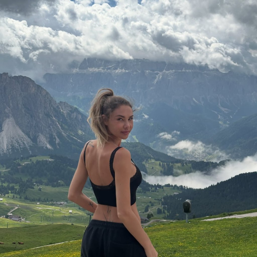 Sahara Ray poses in front of a mountain landscape.